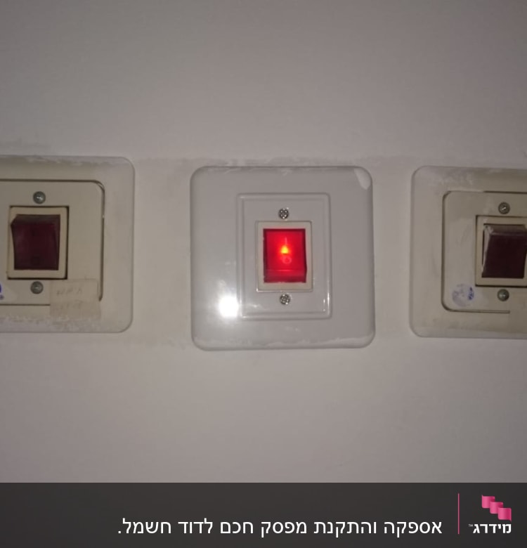 שלושה מתגים חשמליים על קיר, אחד מואר באדום